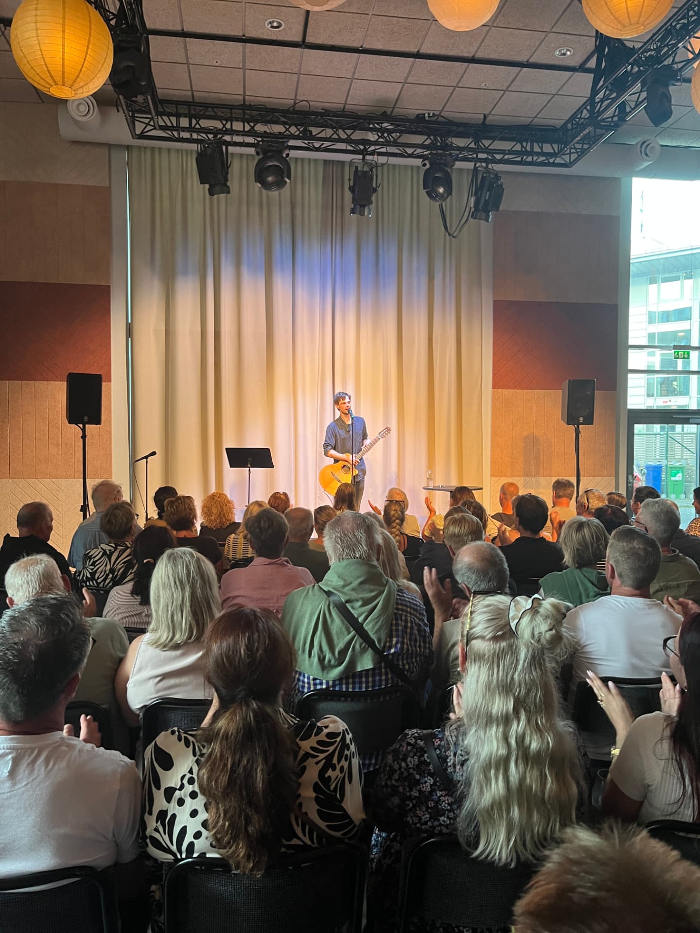 Artist med akustisk gitarr på scen medan publiken applåderar