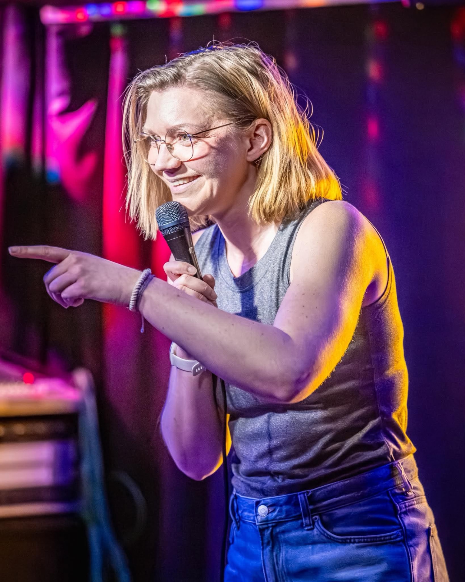 Sanna Mac Donald med mikrofon på scen i färgstarkt scenljus