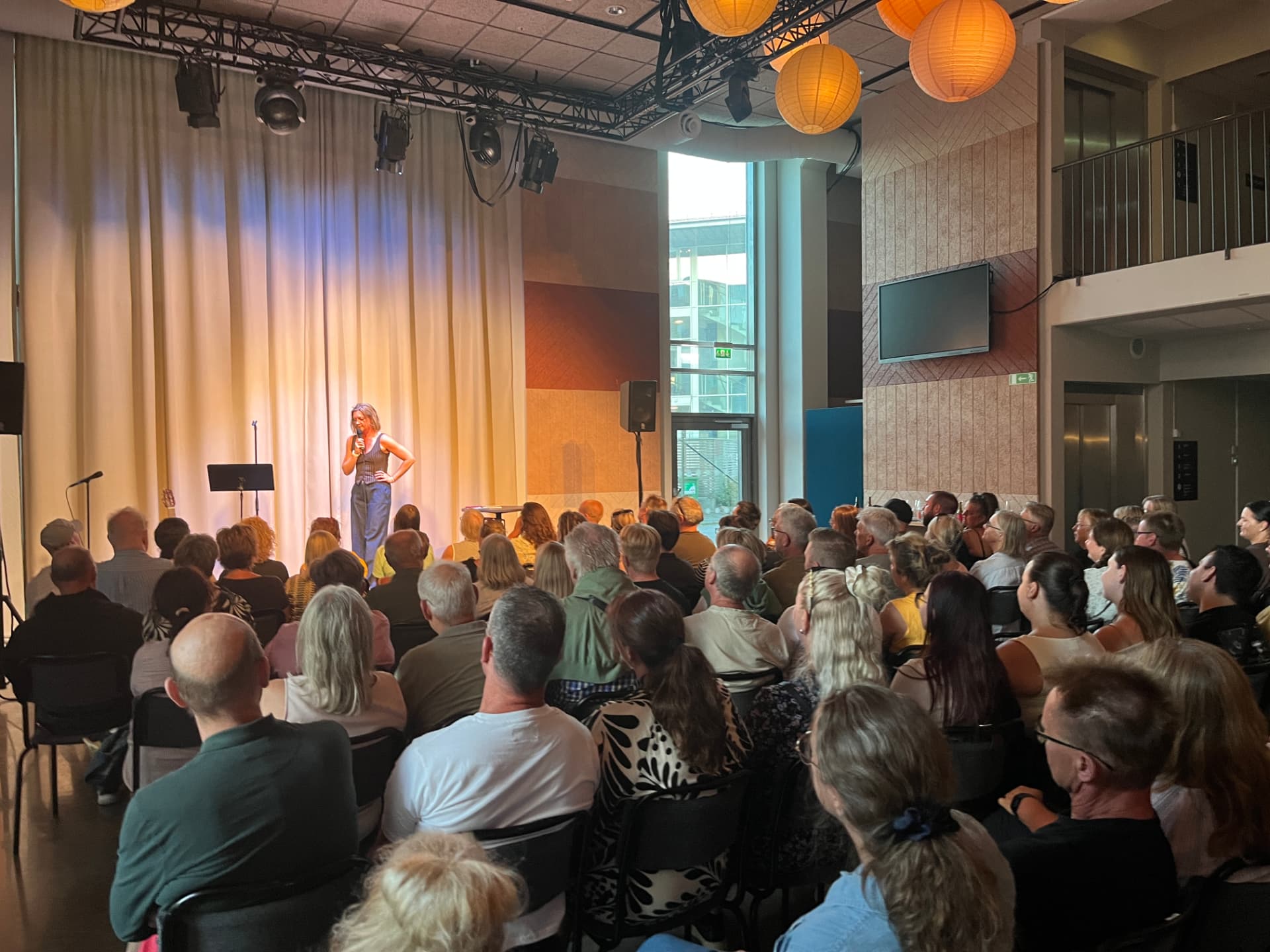 Komiker på scen i varmt scenljus med publik i förgrunden