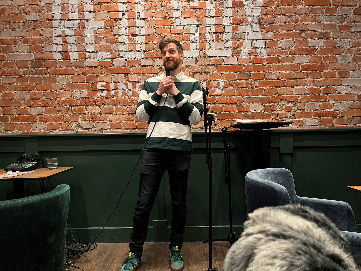 Fredrik Jonsson med mikrofon på scen framför en tegelvägg