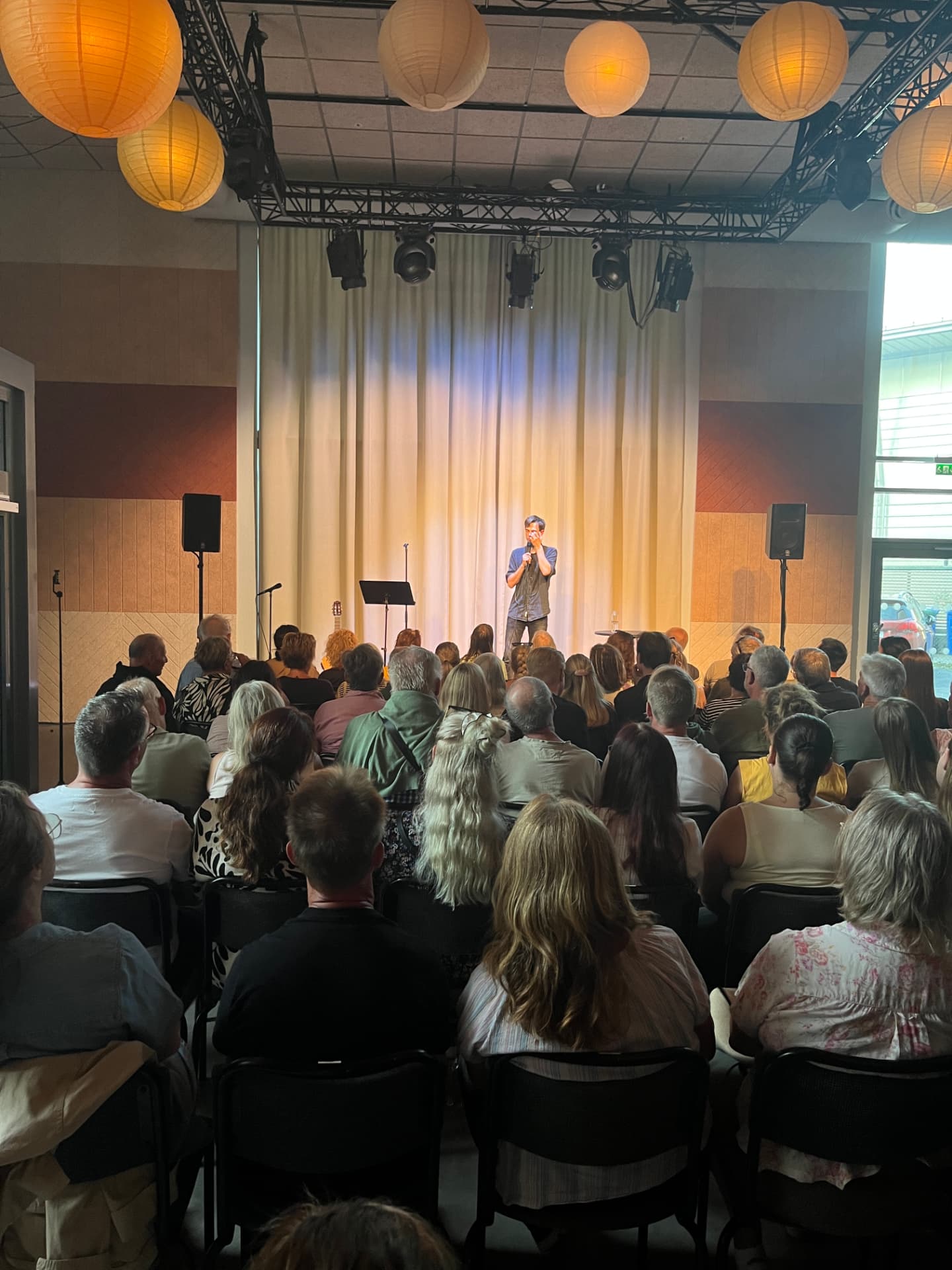 Komiker med mikrofon mitt på scenen framför en stor publik